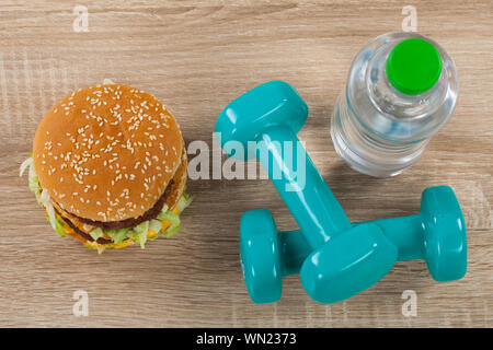 Vista superiore della succosa cheeseburger, ancora acqua blu e manubri - Dieta e fitness vs calorie, fast food Foto Stock