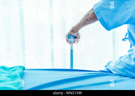 Mano di uomo anziano con metallo bastone mentre è seduto sul letto paziente in ospedale. Settore medicale e della salute custode aiutando concetto senior. copia s Foto Stock