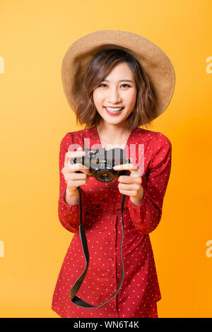 Felice ragazza asiatica guardando la sua fotocamera mentre indossa l'abito rosso e hat isolato su sfondo arancione. Foto Stock