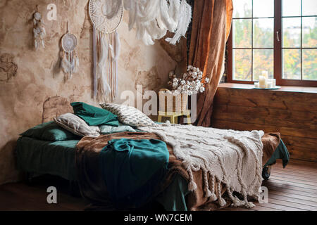 Elegante sala interna con letto grande e confortevole. Beige e bianco sogno catturatori e piume appeso sopra gypsy o hippie slyle bed in dark autunno Foto Stock