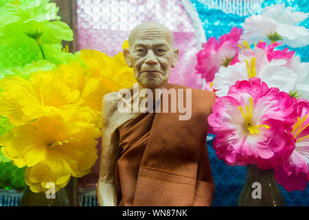 Un sorridente Monaco di cera figura con fiori di Wat Saen Suk in Bang Saen, vicino a Bangkok, Thailandia. Foto Stock