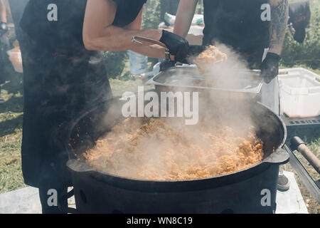 Gli uomini di mettere pilaf dal calderone nel contenitore. Foto Stock