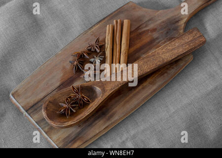 Anice stellato in cucchiaio di legno con cannella sul tagliere di legno. Spezie aromatiche Foto Stock