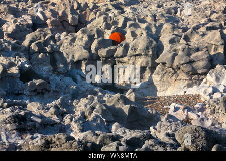 Una lavata a Riva acciaio cava boa o rete da pesca galleggiante realizzato in acciaio e totalmente bloccato in una fessura sulle rocce della spiaggia locale. Foto Stock