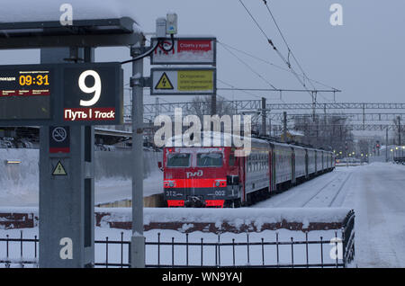 Vitebsky stazione ferroviaria,Saint Petersburg, Russia - 24 Gennaio 2019: rosso-arancione treno ricoperta di neve è il nono titolo è indicato sulla lumin Foto Stock