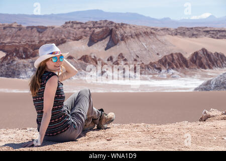 Bionda e giovane donna caucasica da sola seduta e ammirando la natura incontaminata della Valle della Luna nel Deserto di Atacama, Cile. Straordinario paesaggio sfondo con Foto Stock