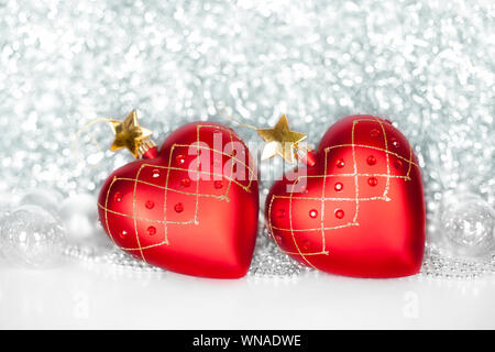 Due red albero di Natale palle di vetro a forma di cuore con stelle d'oro e argento sfere sul lucido tinsel spumanti sfondo Foto Stock
