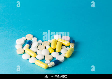 Medicinali bianco, giallo, rotondo blu a forma di cuore pillole su sfondo blu Foto Stock