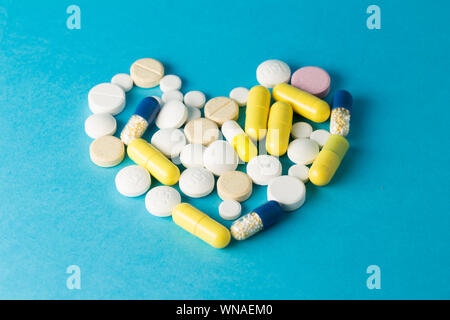 Medicinali bianco, giallo, rotondo blu a forma di cuore pillole su sfondo blu Foto Stock