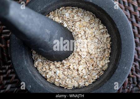 Close-up con tutta schiacciata di avena. In mortaio di pietra. Aspetto rustico. Foto Stock