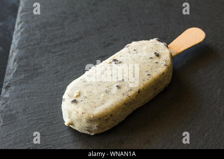 Gelato per lecca-lecca con il cioccolato bianco rivestimento e buio di biscotti al cioccolato sbriciolati isolati su sfondo nero Foto Stock