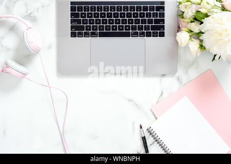 Moderno ufficio in marmo scrivania con computer portatile, blocco di carta e penna, bouquet di rose fiori, cuffie minimo piatto stile laici composizione con Foto Stock