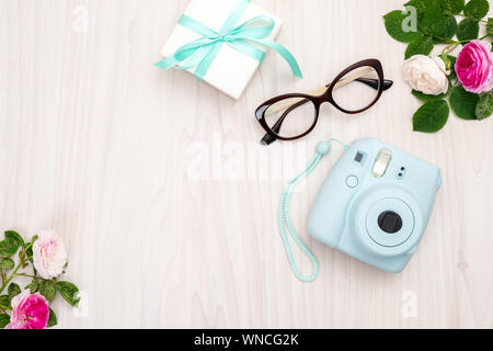 Moderna fotocamera polaroid confezione regalo, bicchieri, accessori femminili, rose su sfondo di legno. Vista superiore, offerta minima piatto stile laici composizione. Donn Foto Stock