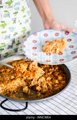 Primo piano di un giovane uomo caucasico di servire un piatto di pollo spagnolo paella, dalla paellera, la padella per paella, cucinata fresca Foto Stock