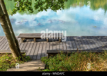 Panca che si affaccia sul fiume Marne su cui un cielo blu con nuvole sono riflettenti. Presi nel tardo pomeriggio a Nogent-sur-Marne, Francia Foto Stock
