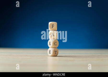 Impilate i cubi di legno tenendo un fake a segno con il fondo due passando per scrivere la parola fatto. Su sfondo blu scuro. Foto Stock