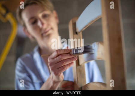 Donna matura Upcycling mobili in officina a casa pittura sedia in legno Foto Stock