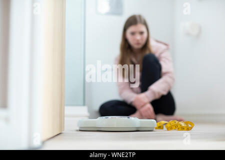 Infelice ragazza seduta nel bagno guardando le scale e il nastro di misurazione Foto Stock