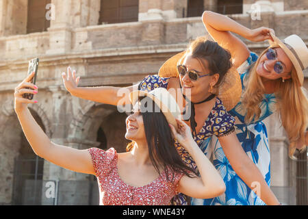 Tre felici donne giovani amici turisti tenendo selfies al Colosseo a Roma, Italia di sunrise. Foto Stock