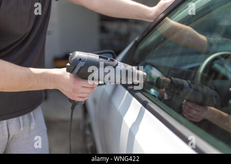 Lavoratore rimozione auto finestra foglio di pellicola utilizzando la pistola ad aria calda. Foto Stock