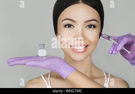 Bella donna asiatica pubblicità iniezioni di bellezza su sfondo grigio. Close-up di anti-invecchiamento iniezione di faccia e la lotta contro la ruga Foto Stock