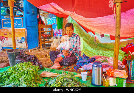 TAUNGGYI, MYANMAR - 20 febbraio 2018: il venditore con il bambino nelle braccia vende verdure e insalate verdi nel mercato degli agricoltori, il 20 febbraio a Taunggyi. Foto Stock