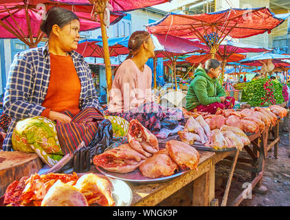 TAUNGGYI, MYANMAR - Febbraio 20, 2018: la linea delle piccole macellerie bancarelle del mercato agricolo con cumuli di pollo su vassoi e fornitori, sittin Foto Stock