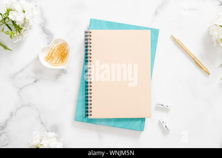 Casa moderna scrivania in ufficio area di lavoro con fogli di carta bianca notebook, fiori bianchi e accessori femminili su sfondo marmo. Appartamento laico, vista dall'alto, overhead Foto Stock