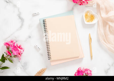 Carta bianca notebook, fiori di colore rosa pastello, coperta e accessori d'oro su sfondo marmo. Appartamento laico, vista dall'alto rose gold home office desk. Bellezza Foto Stock