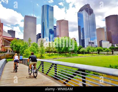 I ciclisti attraversare ponte di legno in Buffalo Bayou Park, con una splendida vista del centro cittadino di Houston (skyline / grattacieli) in background su un giorno di estate Foto Stock