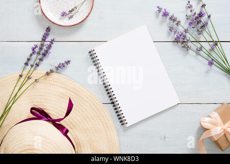 Flatlay di home office desk area di lavoro con la carta notebook, cappello di paglia, di fiori di lavanda, confezione regalo. Fashion blogger summer floral concetto di lavoro. Foto Stock