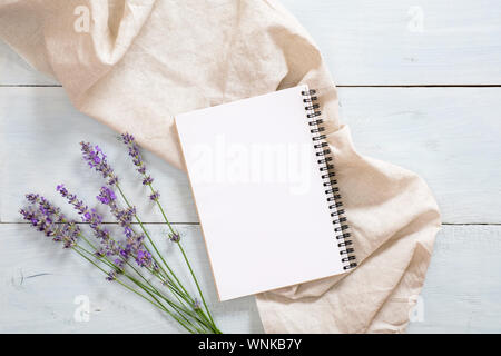 Composizione Flatlay con carta bianca in Blocco note di fiori di lavanda, pastello beige coperta su rustiche in legno di colore blu sullo sfondo. Appartamento laico, vista dall'alto ancora vita co Foto Stock