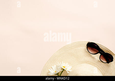 Composizione Flatlay con cappello di paglia, daisy fiori e occhiali da sole sul rosa pastello sfondo. Appartamento laico, vista dall'alto, copia dello spazio. Moda estate, vacanze c Foto Stock