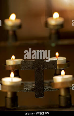 Candele accese nella chiesa con ferro realizzato cross Foto Stock