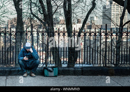 Lonely guy fissando il suo telefono mentre è seduto sulla strada Foto Stock