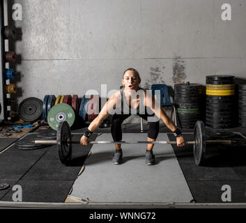Forte giovane donna nella formazione grungy palestra con pesi pesanti. Foto Stock