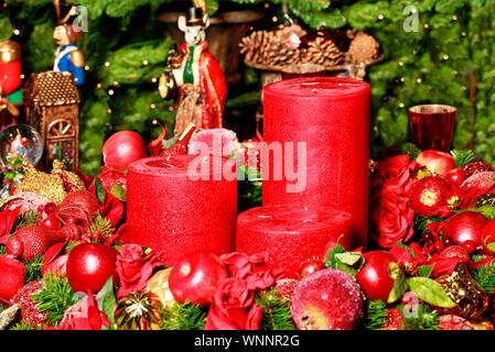 Decorazione di Natale: spessa tre candele rosse circondato da sfocata decorazioni natalizie e personaggi delle fiabe sullo sfondo dei rami di abete, clos Foto Stock