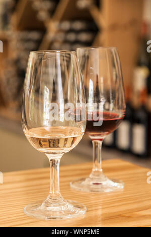 Bicchieri di vino rosso e bianco sul tavolo bar in cantina sala degustazione con bottiglie di vino in background Foto Stock