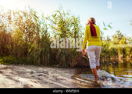 Di mezza età nudi donna camminando sulla riva del fiume sulla giornata d'autunno. Senior lady divertirsi nella foresta e godere la natura Foto Stock