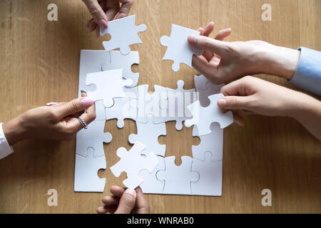 Vista dall'alto di diverse persone assemblare il puzzle alla ricerca di soluzione Foto Stock