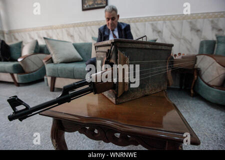 Baghdad in Iraq. 06 Sep, 2019. Insegnante di iracheni e musicista Majed Abdennour rimane dietro uno strumento musicale realizzato da un kalashnikov fucile da assalto e una scatola di munizioni. Abdennour aveva il Kalashnikov a casa tra il 2006 e il 2008 per proteggere la sua famiglia durante la violenza settaria tra le milizie e gli estremisti di iracheni di sunniti e sciiti fazioni. Dopo più di dieci anni di abbandonare la sua arma, Abdennour ha deciso di portarlo a un carpentiere metallico per trasformarlo in uno strumento musicale che esegue come un liuto. Credito: Ameer Al Mohammedaw/dpa/Alamy Live News Foto Stock