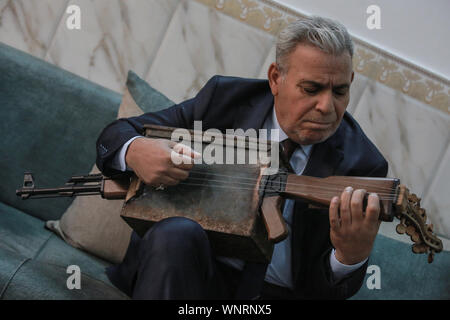 Baghdad in Iraq. 06 Sep, 2019. Insegnante di iracheni e musicista Majed Abdennour suona uno strumento musicale realizzato da un kalashnikov fucile da assalto e una scatola di munizioni. Abdennour aveva il Kalashnikov a casa tra il 2006 e il 2008 per proteggere la sua famiglia durante la violenza settaria tra le milizie e gli estremisti di iracheni di sunniti e sciiti fazioni. Dopo più di dieci anni di abbandonare la sua arma, Abdennour ha deciso di portarlo a un carpentiere metallico per trasformarlo in uno strumento musicale che esegue come un liuto. Credito: Ameer Al Mohammedaw/dpa/Alamy Live News Foto Stock