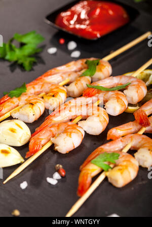 Gamberetti gamberetti con limone, aglio ed erbe aromatiche sulla pietra nera dello sfondo. Primo piano Foto Stock