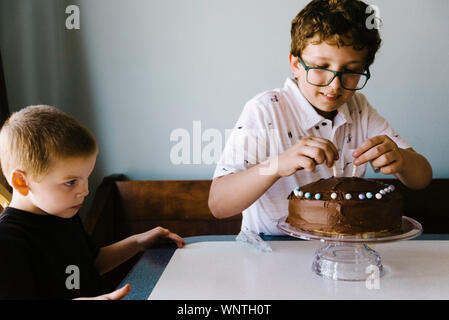 Tween boy decorare la sua torta di compleanno a casa con il nipote. Foto Stock