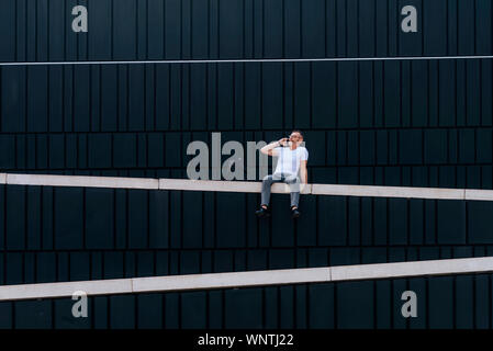 Ritratto di maturo uomo barbuto al telefono seduto su un muro esterno Foto Stock