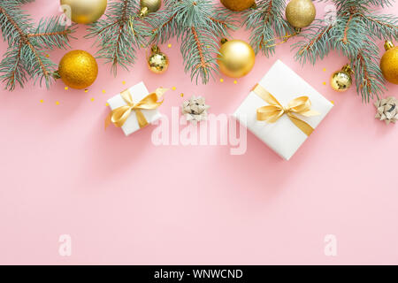 Telaio di Natale confine con abete rami, Natale palline dorate, presenta sul rosa pastello sfondo. Appartamento laico, vista dall'alto. Foto Stock