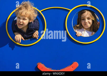 Un ragazzo e una ragazza loll presso il parco giochi. Due bambini rendendo grimace e divertirsi al parco giochi. Male Naughty kids concetto. Foto Stock