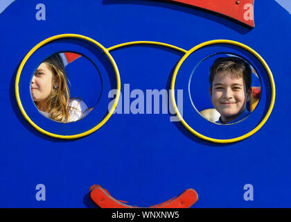 Due bambini spiata attraverso il foro sul playhouse. Un ragazzo e una ragazza a giocare nel parco. Dei bambini felici concetto. Foto Stock