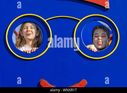 Un ragazzo e una ragazza loll presso il parco giochi. Due bambini rendendo grimace e divertirsi al parco giochi. Male Naughty kids concetto. Foto Stock