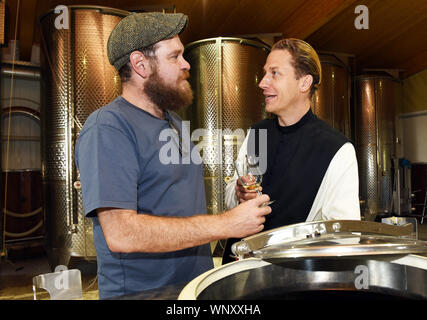 04 settembre 2019, della Renania settentrionale-Vestfalia, Bochum: Padre Justinus (r) ed il distillatore Christof Hans sono in piedi in distilleria degustazione gin. Nella sua produzione egli produce una elevata percentuale di gin e lo chiama "onatic dry gin'. Le erbe aromatiche di cui ha bisogno sono piantate e coltivate nel giardino del monastero. Egli riceve il ginepro provenienti dalla Toscana e il grano da cui l'alcool è ottenuto egli riceve dalla madre Abbazia di Heiligenkreuz nella Foresta Viennese. Nel monastero stesso egli non è permesso di bruciare qualsiasi gin perché non hanno alcun diritto di distillazione. Per questo egli unità ad un produttore nelle vicinanze (di Foto Stock